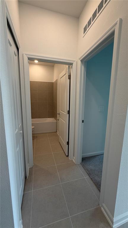 A hallway with tile flooring connects to a bathroom with a tub and a carpeted room — 6044 MEDITATION DRIVE, CLERMONT, FL