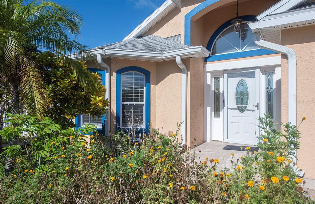 The exterior of a tan house features blue window trim, a white door, and landscaping — 1150 OAKWOOD DRIVE, DUNEDIN, FL