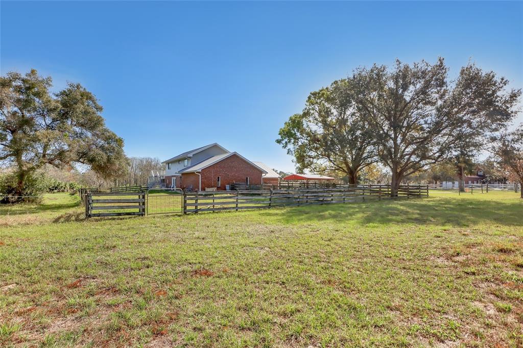 A brick house sits behind a wooden fence in a large, grassy field with trees — 5005 HIGHWAY 1, MIMS, FL