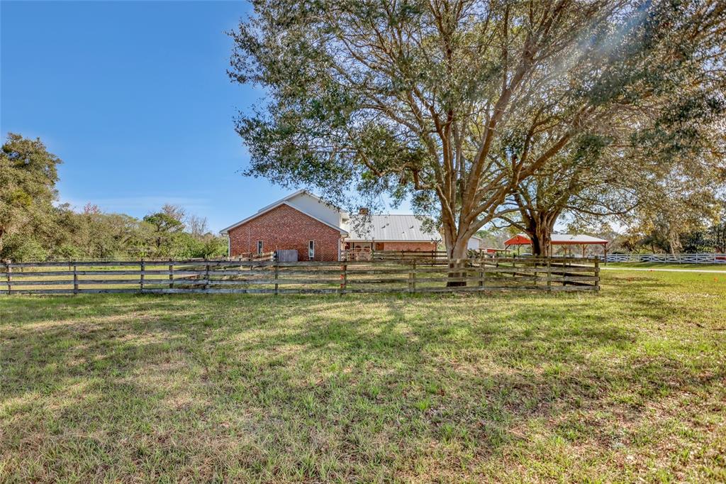 A brick house sits behind a wooden fence with large trees in the yard — 5005 HIGHWAY 1, MIMS, FL