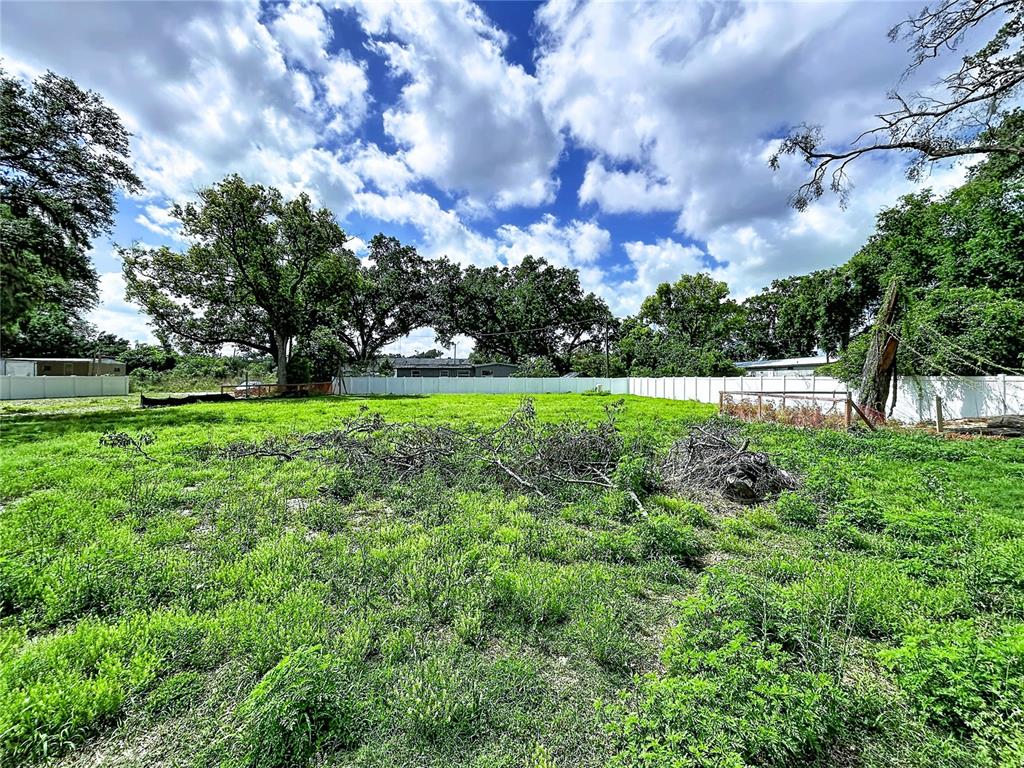A grassy, vacant lot features scattered tree branches and is enclosed by a white fence — ROBSON, SEFFNER, FL