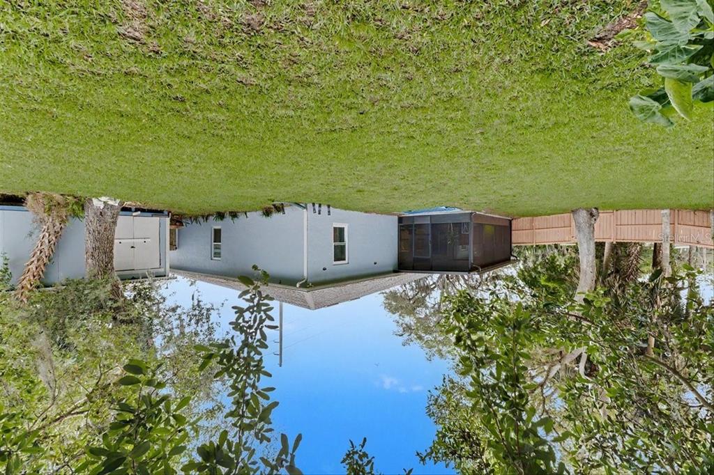 A light blue house with a screened-in porch sits in a large, grassy backyard — 1830 ORANGE TREE DRIVE, EDGEWATER, FL