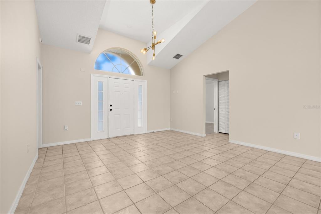 An empty foyer with beige tile flooring, a vaulted ceiling, and a white front door — 3141 ENCLAVE COURT, KISSIMMEE, FL
