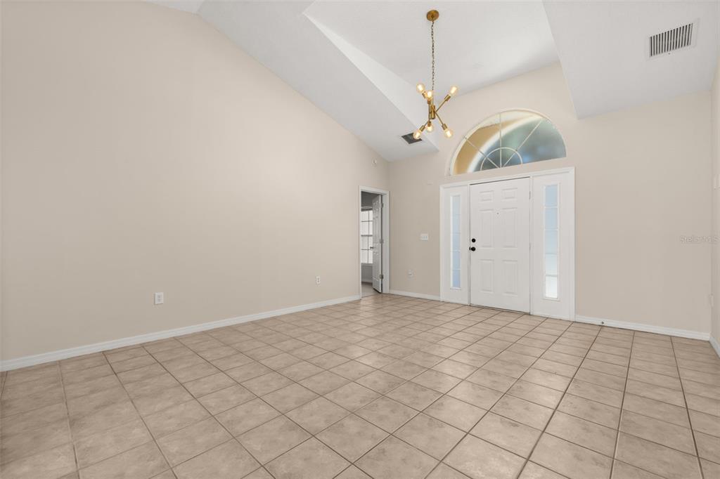 An empty room with vaulted ceilings, tile flooring, a chandelier, and a front entryway door — 3141 ENCLAVE COURT, KISSIMMEE, FL