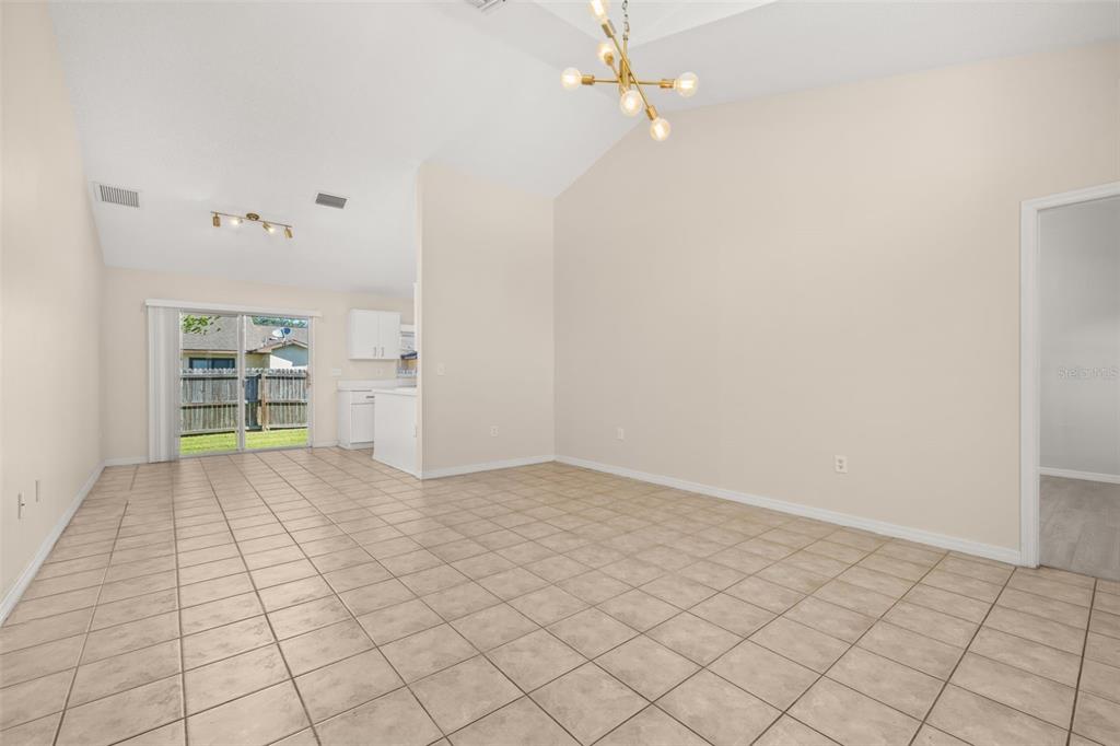 An empty room with beige tile flooring, vaulted ceilings, and a sliding glass door — 3141 ENCLAVE COURT, KISSIMMEE, FL