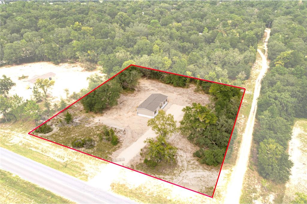 An aerial view shows a single-story house situated on a large, partially cleared, wooded lot — 11031 NE 80 AVENUE, BRONSON, FL