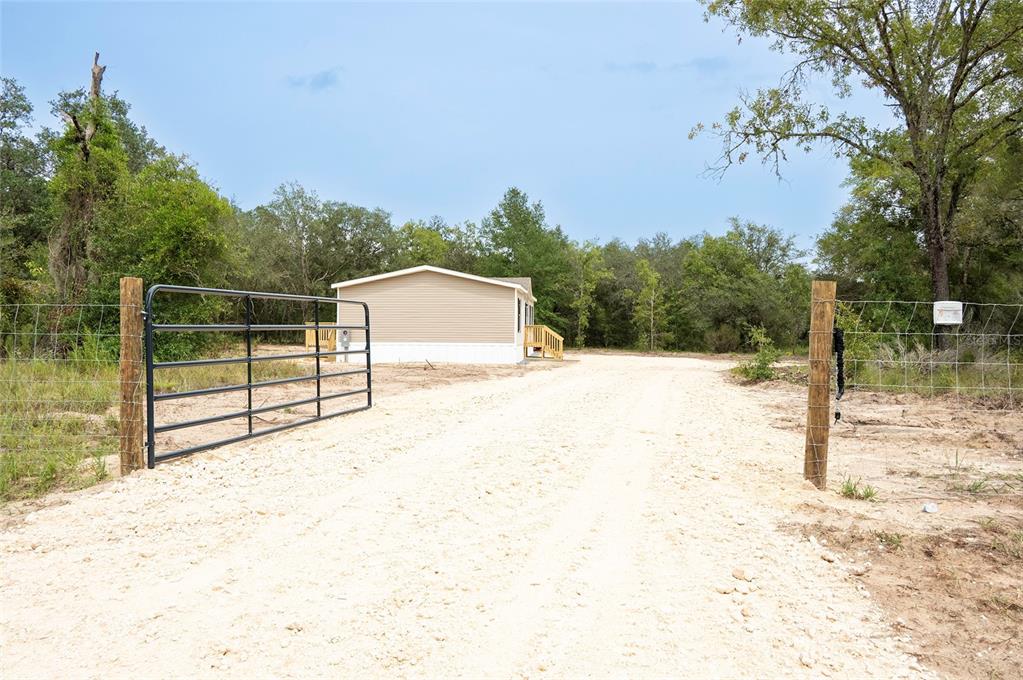 A beige mobile home sits behind a metal gate at the end of a gravel driveway — 11031 NE 80 AVENUE, BRONSON, FL