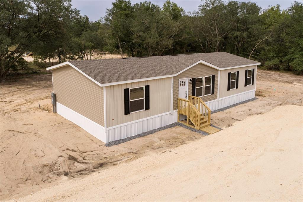 A tan manufactured home with a brown shingled roof sits on a sandy, undeveloped lot — 11031 NE 80 AVENUE, BRONSON, FL