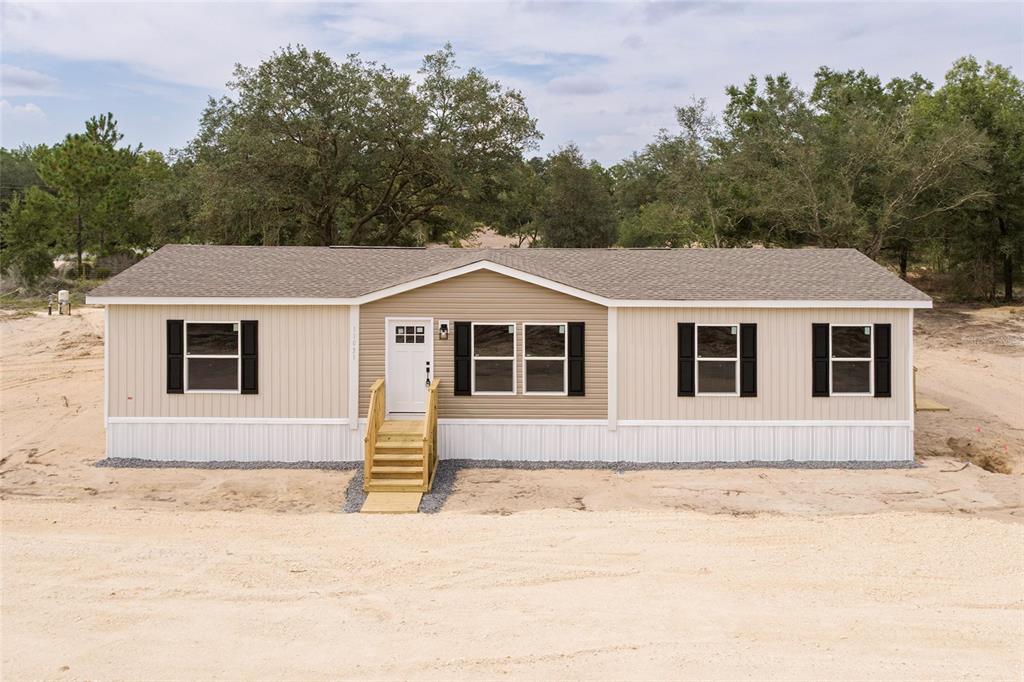 A single-story manufactured home with tan siding, black shutters, and wooden front steps — 11031 NE 80 AVENUE, BRONSON, FL