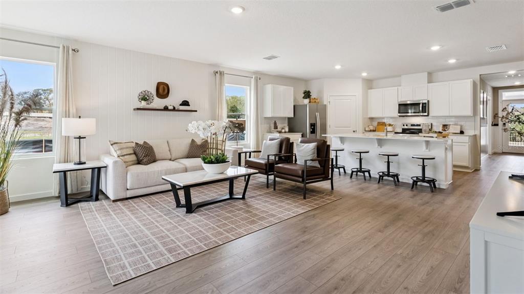 An open-concept living room and kitchen feature white cabinetry, wood-look flooring, and modern furniture — 1144 GULL DRIVE, APOPKA, FL