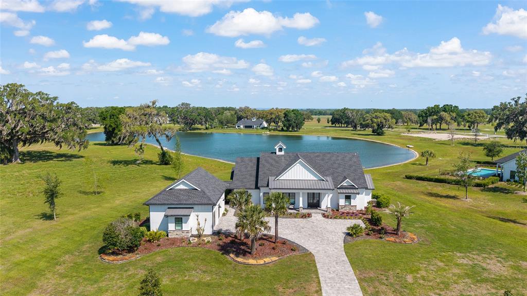 An aerial view shows a white farmhouse with a dark roof beside a large pond — 12902 SW 138TH LOOP, DUNNELLON, FL