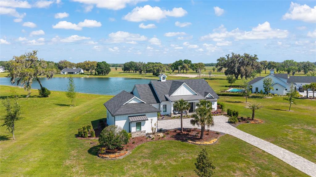 An aerial view shows a white farmhouse with a dark roof beside a large pond — 12902 SW 138TH LOOP, DUNNELLON, FL