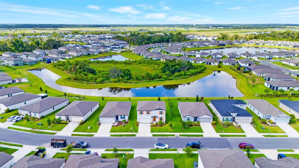 An aerial view shows a suburban neighborhood with houses surrounding a central pond — 10025 DAYBREAK GLEN, PARRISH, FL