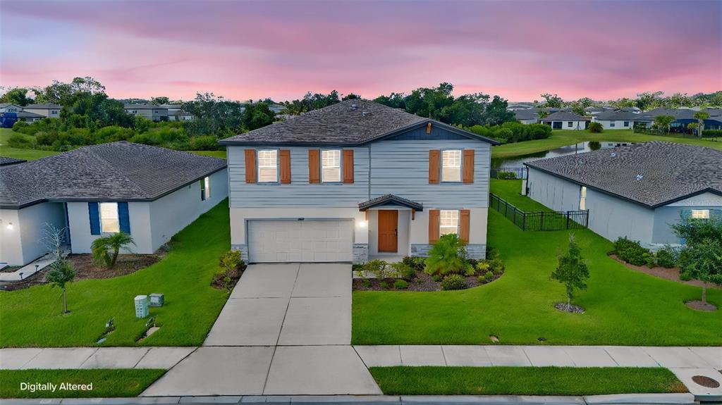 The rear exterior of a two-story house features a large lawn and a sliding glass door — 10025 DAYBREAK GLEN, PARRISH, FL