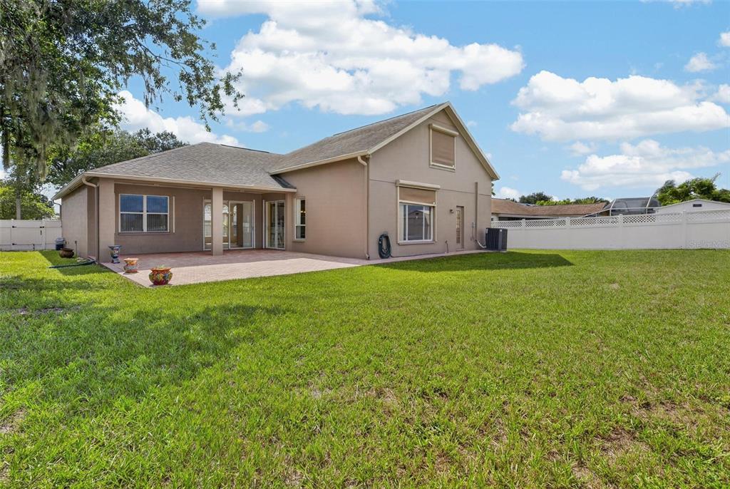 The exterior of a tan house features a paved patio and a large grassy backyard — 10303 TARRAGON DRIVE, RIVERVIEW, FL