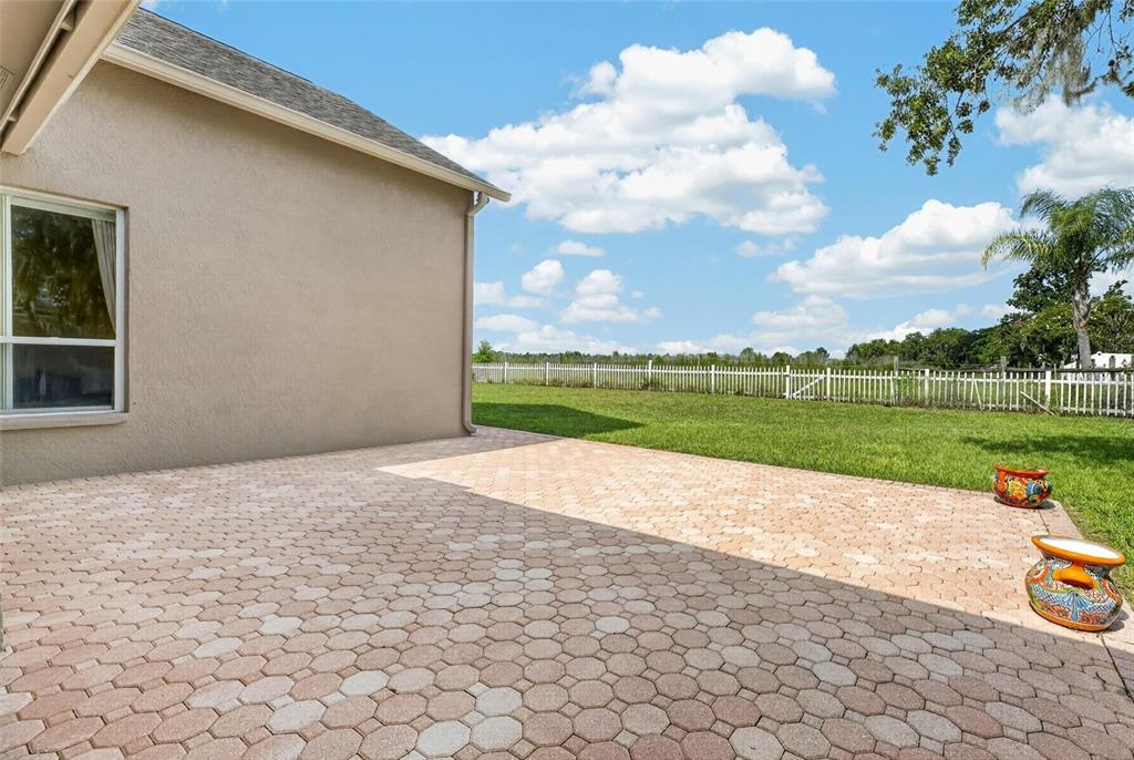 A paved patio extends from the side of a house toward a fenced grassy yard — 10303 TARRAGON DRIVE, RIVERVIEW, FL