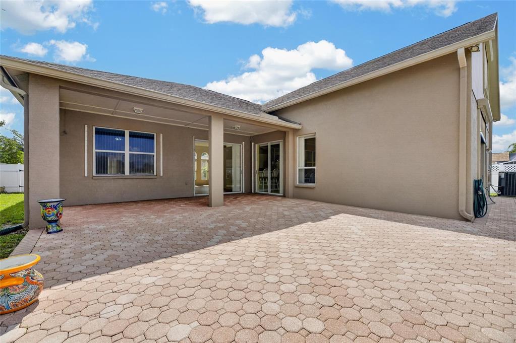 A paved patio area sits beneath a covered porch attached to a beige stucco house — 10303 TARRAGON DRIVE, RIVERVIEW, FL