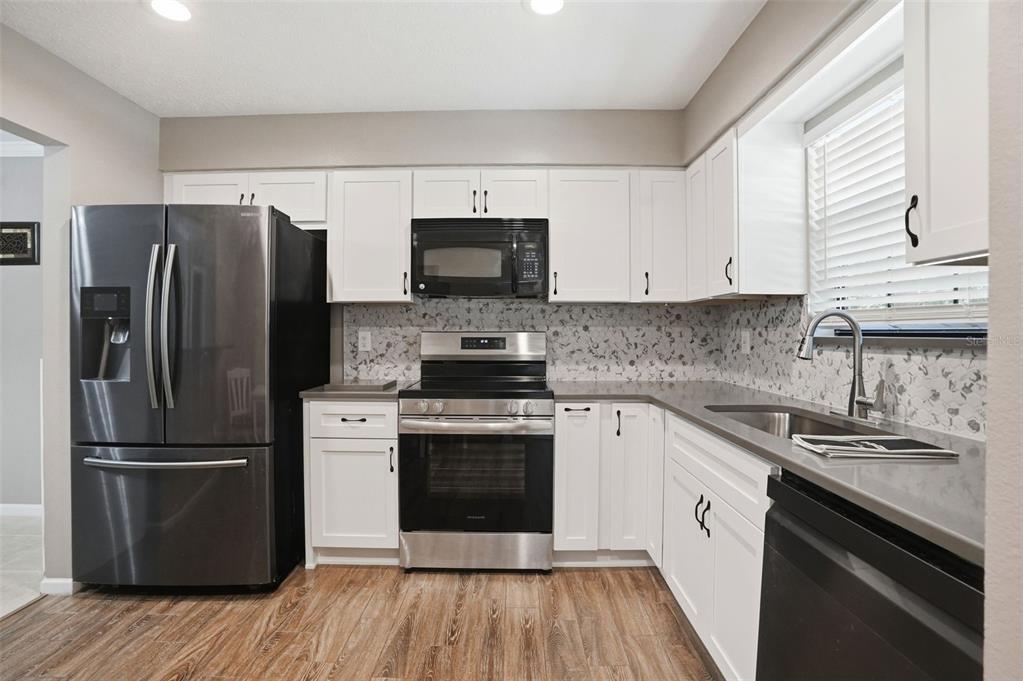 A kitchen features white cabinets, stainless steel appliances, a patterned backsplash, and wood-look flooring — 913 CANDLEBROOK LANE, BROOKSVILLE, FL