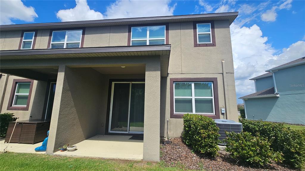 The exterior of a two-story stucco home features a covered patio and a sliding glass door — 11840 SKY ACRES TERRACE, BRADENTON, FL