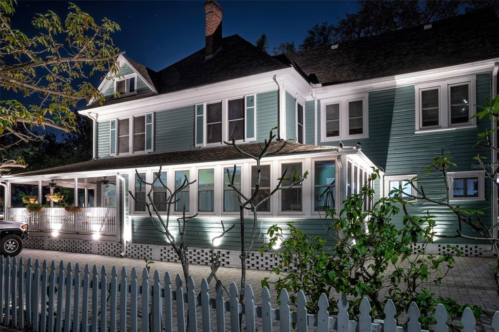 A two-story teal house with a wrap-around porch and white picket fence at night — 304 15TH STREET W, BRADENTON, FL