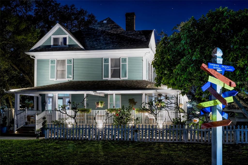 A two-story, light green Victorian-style house at night with a wrap-around porch and picket fence — 304 15TH STREET W, BRADENTON, FL