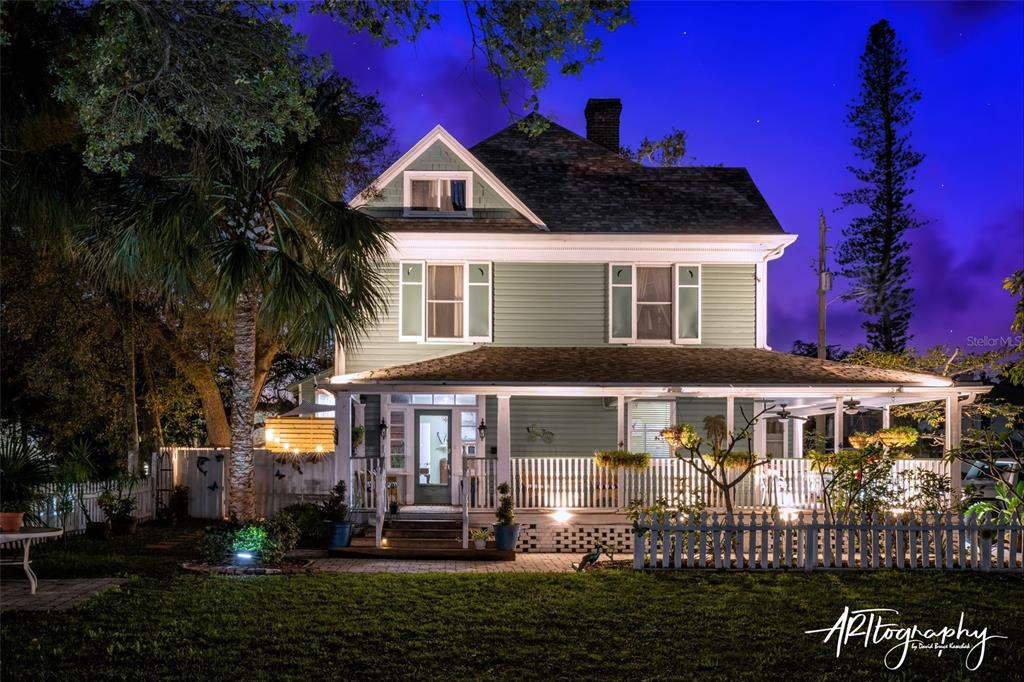 A two-story green house with a wrap-around porch is illuminated at night — 304 15TH STREET W, BRADENTON, FL