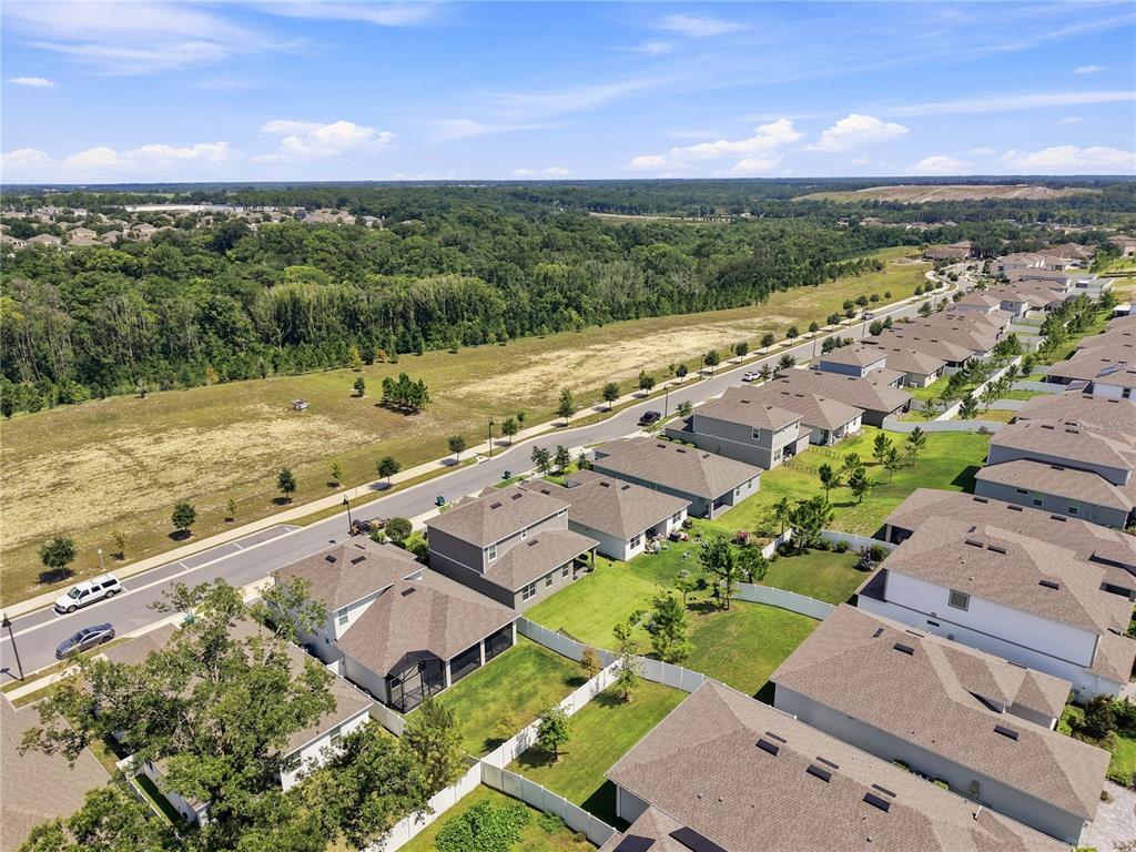 An aerial view shows a suburban neighborhood with houses, fenced backyards, and a nearby road — 2463 NATOMA BOULEVARD, MOUNT DORA, FL