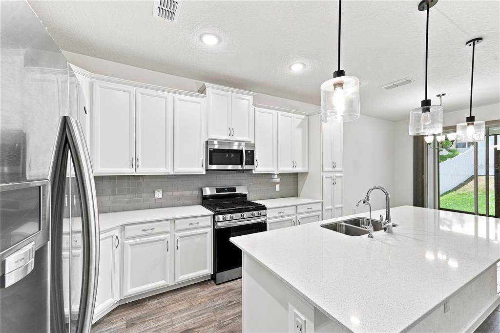 A modern kitchen features white cabinets, stainless steel appliances, a quartz island, and gray backsplash — 2463 NATOMA BOULEVARD, MOUNT DORA, FL