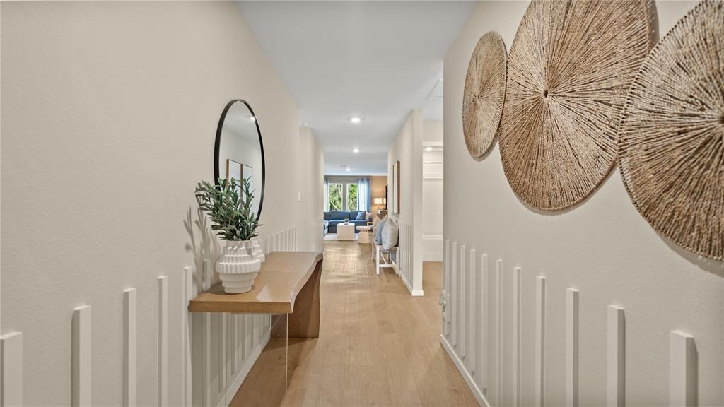 A hallway features light wood flooring, vertical wall slats, a console table, and circular wall decor — 6124 SWAMP BAY DRIVE, EDGEWATER, FL