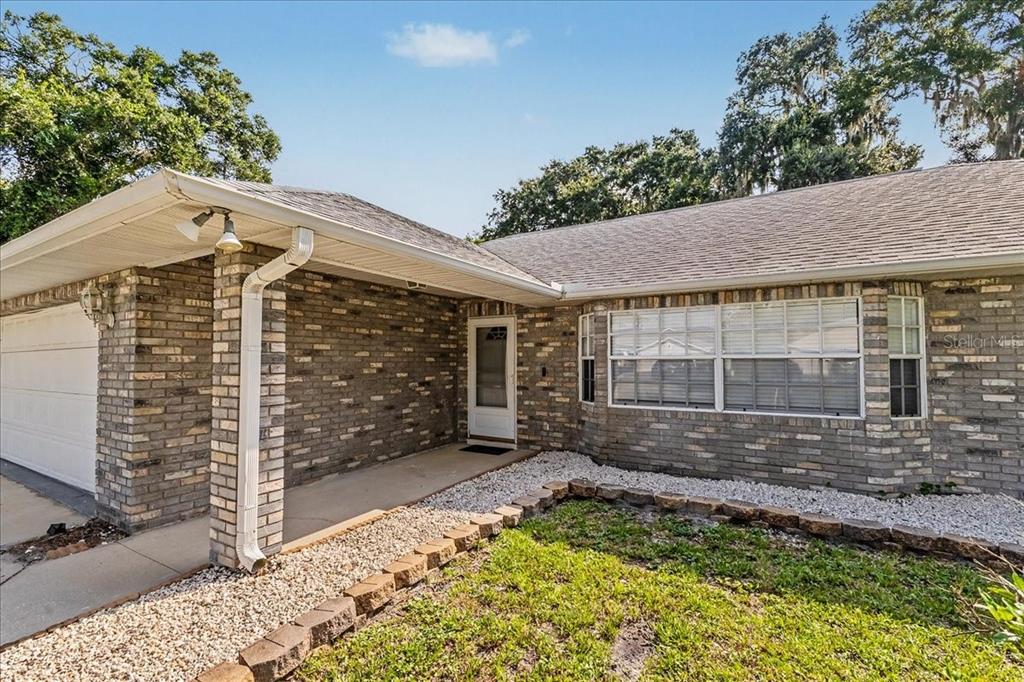 A single-story brick house with a white garage door, front entryway, and a gravel garden bed — 2311 PINE TREE, EDGEWATER, FL
