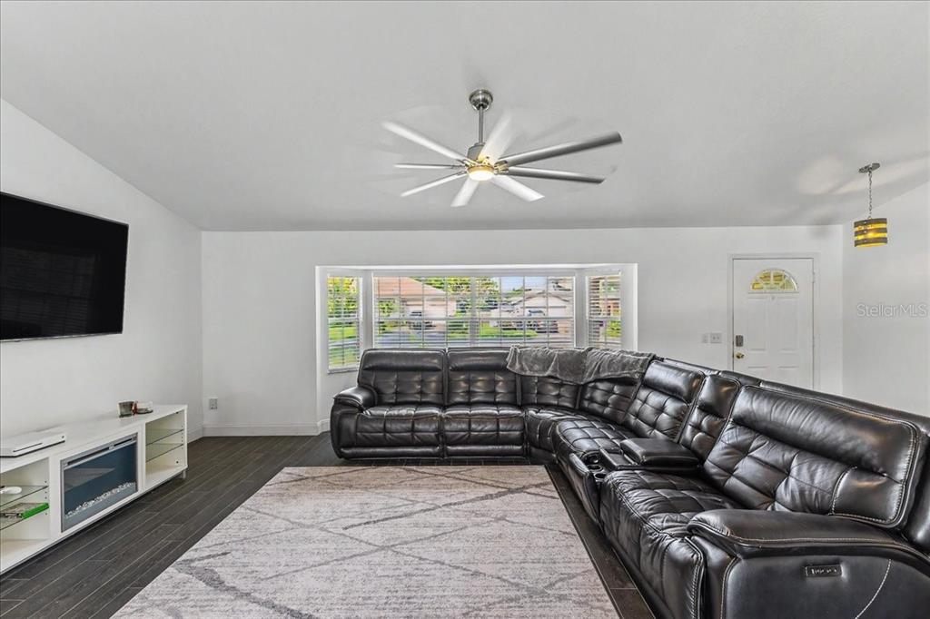 A living room features a large black sectional sofa, a television, and a ceiling fan — 2311 PINE TREE, EDGEWATER, FL