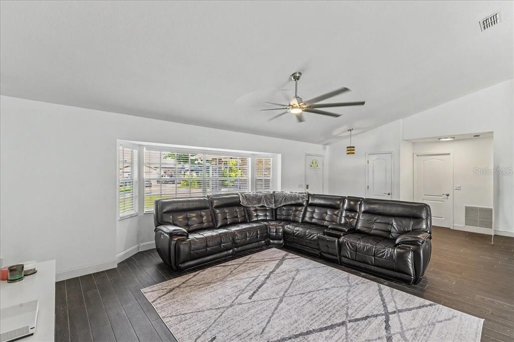 A living room features dark wood floors, a large leather sectional, and a bay window — 2311 PINE TREE, EDGEWATER, FL