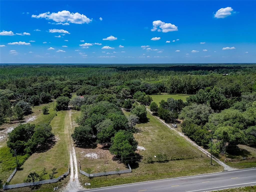 An aerial view shows a rural property with a gravel driveway, fencing, and wooded areas — 7119 STATE ROAD 33, CLERMONT, FL