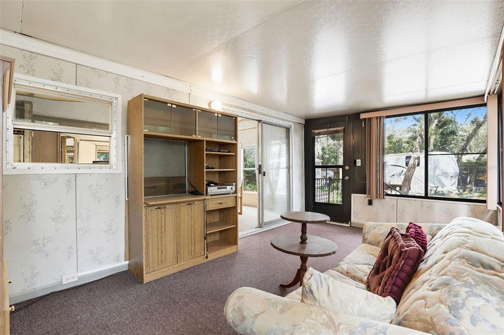 A living room features floral wallpaper, brown carpeting, a wooden entertainment center, and sliding doors — 3000 CLARCONA ROAD UNIT 362, APOPKA, FL