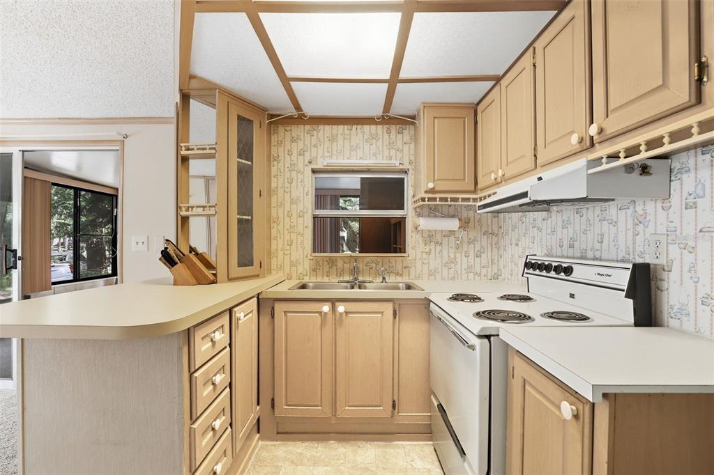A kitchen with light wood cabinets, patterned wallpaper, a white stove, and a drop ceiling — 3000 CLARCONA ROAD UNIT 362, APOPKA, FL