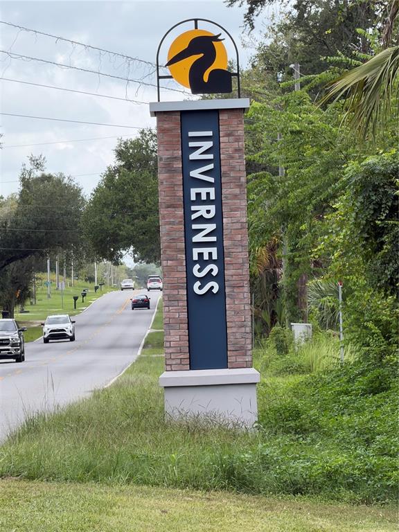 A brick monument sign for Inverness stands beside a road with cars driving in the distance — 3677 E YANDLE PLACE, INVERNESS, FL