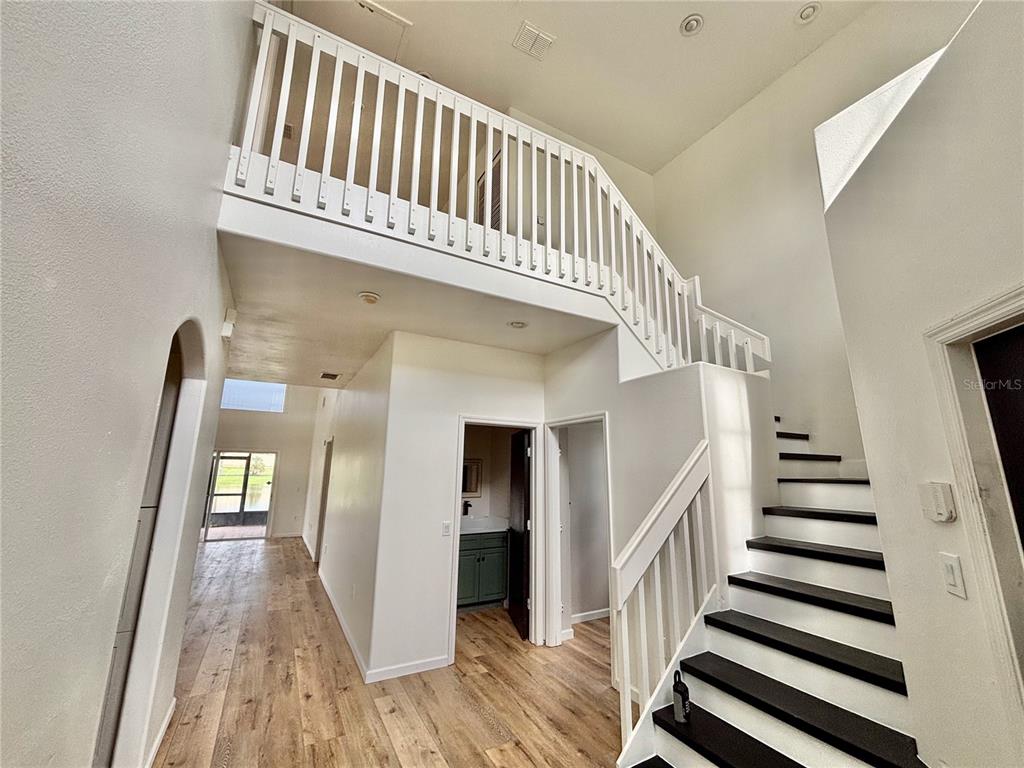 A bright entryway features a staircase with dark treads, white railings, and light wood flooring — 13229 CANNA LILY DRIVE, ORLANDO, FL