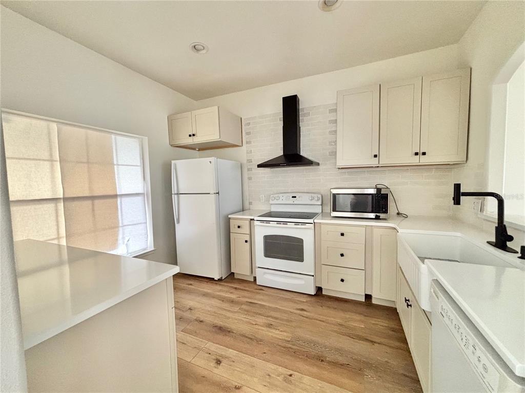 A kitchen features white cabinets, a white refrigerator, a black range hood, and wood flooring — 13229 CANNA LILY DRIVE, ORLANDO, FL