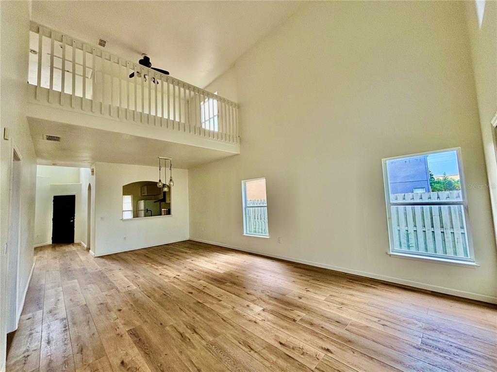 A living room with high ceilings, a loft balcony, and wood-look flooring — 13229 CANNA LILY DRIVE, ORLANDO, FL