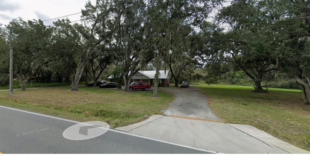 A single-story house sits on a large, tree-covered lot with a gravel driveway — 4040 WARING ROAD, LAKELAND, FL