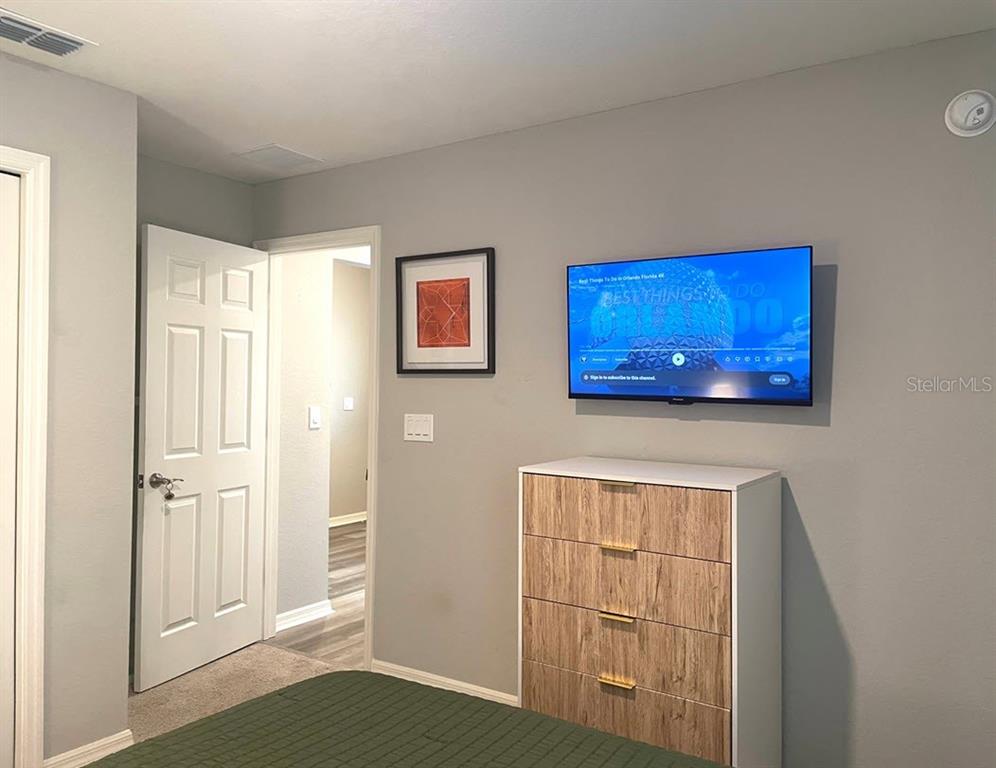 A bedroom features a wall-mounted television above a wooden dresser, a doorway, and framed artwork — 315 LILY LANE, DAVENPORT, FL