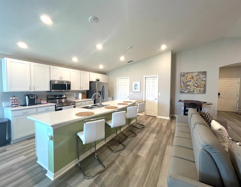 A kitchen with white cabinets, a green island with bar seating, and light wood flooring — 315 LILY LANE, DAVENPORT, FL