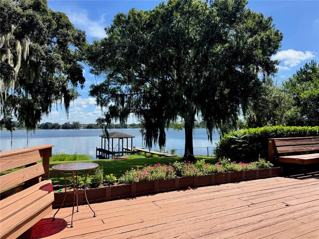A wooden deck overlooks a lake with a dock, large trees, and a flower planter — 2510 CYPRESS GARDENS BOULEVARD, WINTER HAVEN, FL