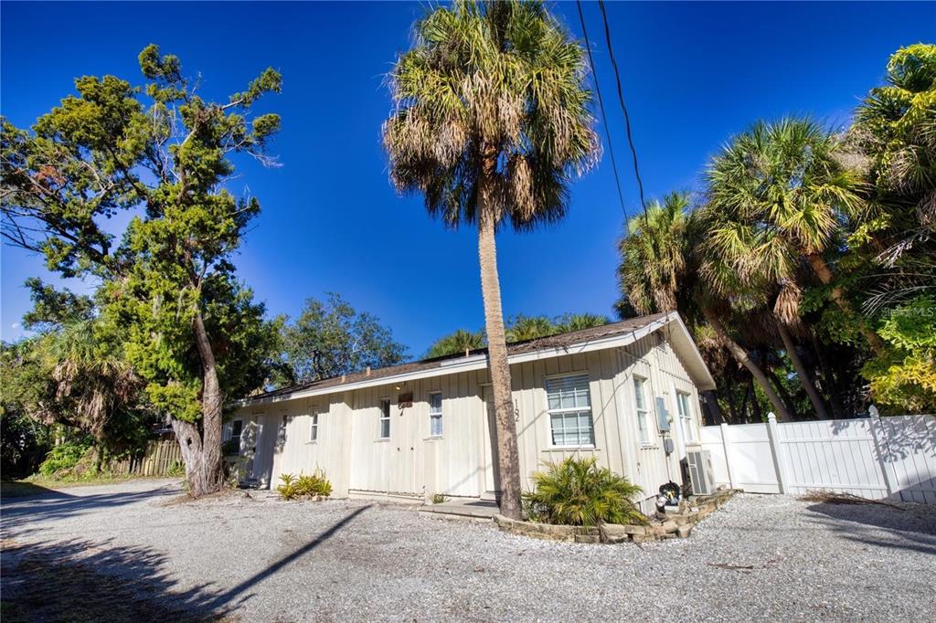 A single-story house with light-colored vertical siding stands on a gravel lot with palm trees — 160 GARDEN LANE, SARASOTA, FL