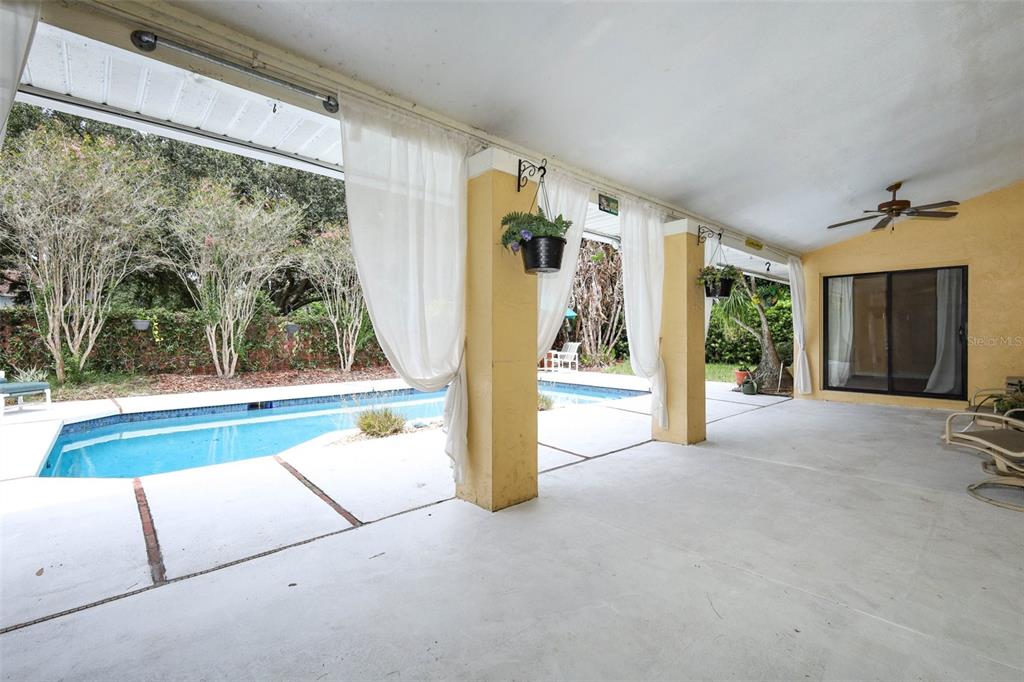 A covered patio with white curtains overlooks a swimming pool and a landscaped backyard — 4661 N SAINT BRIDES CIRCLE, ORLANDO, FL