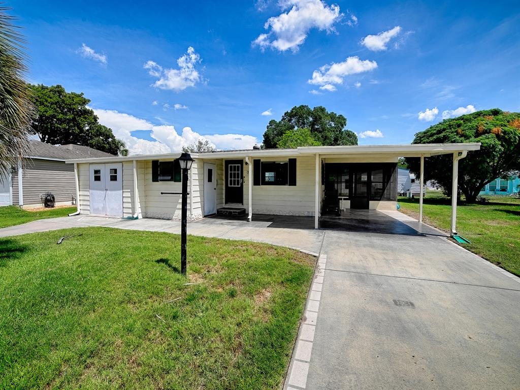 A single-story house with light siding, a carport, and a concrete driveway under a blue sky — 721 SHARON DRIVE, THE VILLAGES, FL