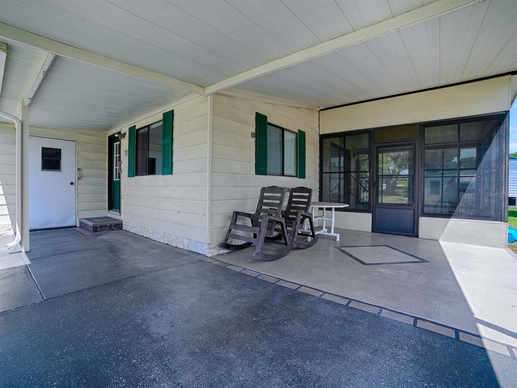 A covered concrete patio features two rocking chairs, a small table, and a screened enclosure — 721 SHARON DRIVE, THE VILLAGES, FL
