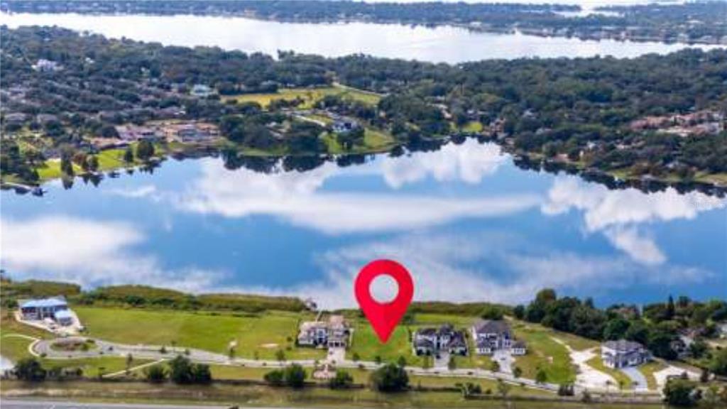 An aerial view shows a vacant waterfront lot marked by a pin between luxury houses — 1330 LAKE OLIVIA, WINDERMERE, FL
