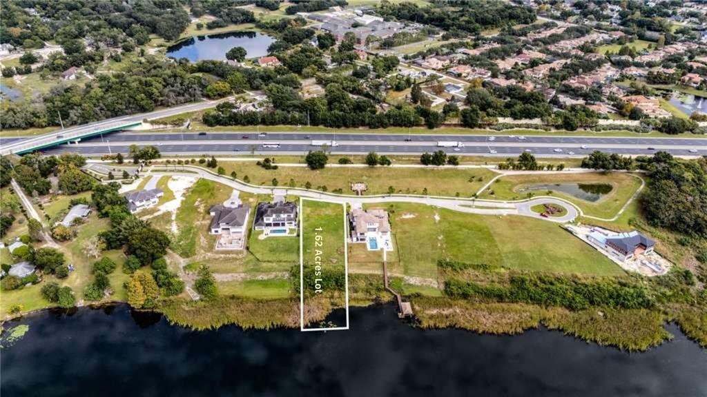An aerial view shows a waterfront residential lot outlined in white near a highway — 1330 LAKE OLIVIA, WINDERMERE, FL