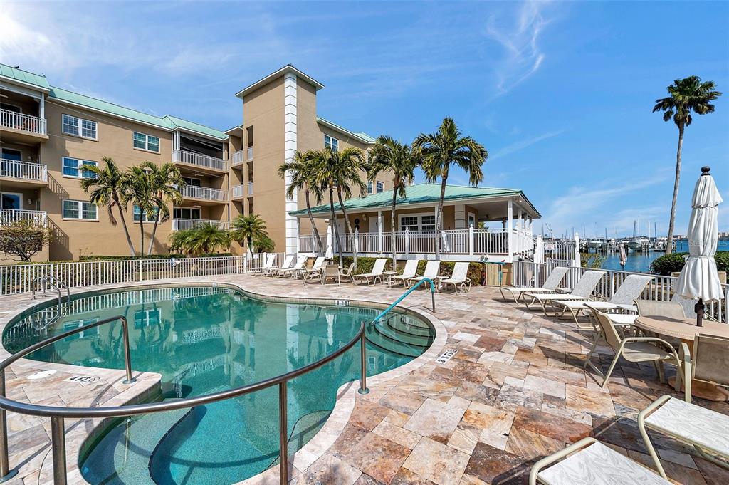 A swimming pool with a stone deck sits in front of a multi-story apartment building — 399 150TH AVENUE UNIT 101, MADEIRA BEACH, FL